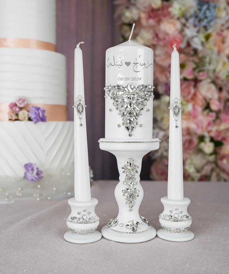 May include: White wedding unity candles with a silver heart and rhinestones. The center candle has the Arabic text "حُبٌّ خَالِدٌ" and the date "08/19/2024".