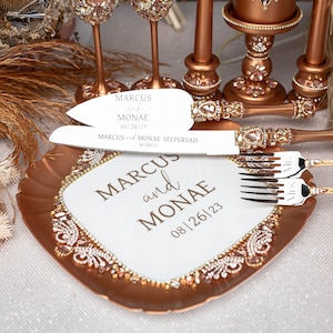 May include: A white cake cutting set with a rose gold handle and a white plate with the text "MARCUS and MONAE 08|26|23" on it.