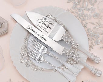 May include: A silver cake knife and server set with two matching forks, featuring handles encrusted with clear crystals. The knife is engraved with "Forever in Love" and the server with "Mr. & Mrs. Pauligoti 08.01.2026 Two hearts, one journey".