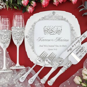 May include: White wedding cake serving set with a decorative plate featuring Arabic calligraphy and the names Kareem & Mariam. The plate also includes the text "And We Created You In Pairs (Quran 78:8)". The set includes two champagne flutes, a cake knife, and two forks with the words "I do" and "Me too" engraved on them.