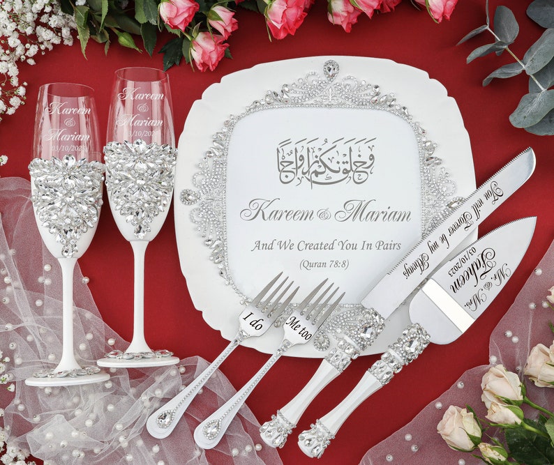 May include: White wedding cake serving set with a decorative plate featuring Arabic calligraphy and the names Kareem & Mariam. The plate also includes the text "And We Created You In Pairs (Quran 78:8)". The set includes two champagne flutes, a cake knife, and two forks with the words "I do" and "Me too" engraved on them.