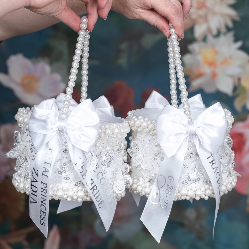 May include: Two white pearl-embellished boxes with satin bows and ribbon handles. The boxes are decorated with lace and have personalized ribbons with the text "Little Bride", "The Coco", "ZADIA", "Royal Princess", "TRACIA", and "6-28-23".