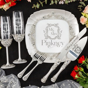 Peut inclure: Un ensemble de mariage comprenant deux flûtes à champagne, une assiette, des fourchettes et des couverts à gâteau. Les articles sont blancs et argentés, avec des ornements en cristal. L'assiette et les flûtes sont gravées de "Mr. & Mrs. Pinkney". Les couverts à gâteau sont gravés de "Always & Forever".