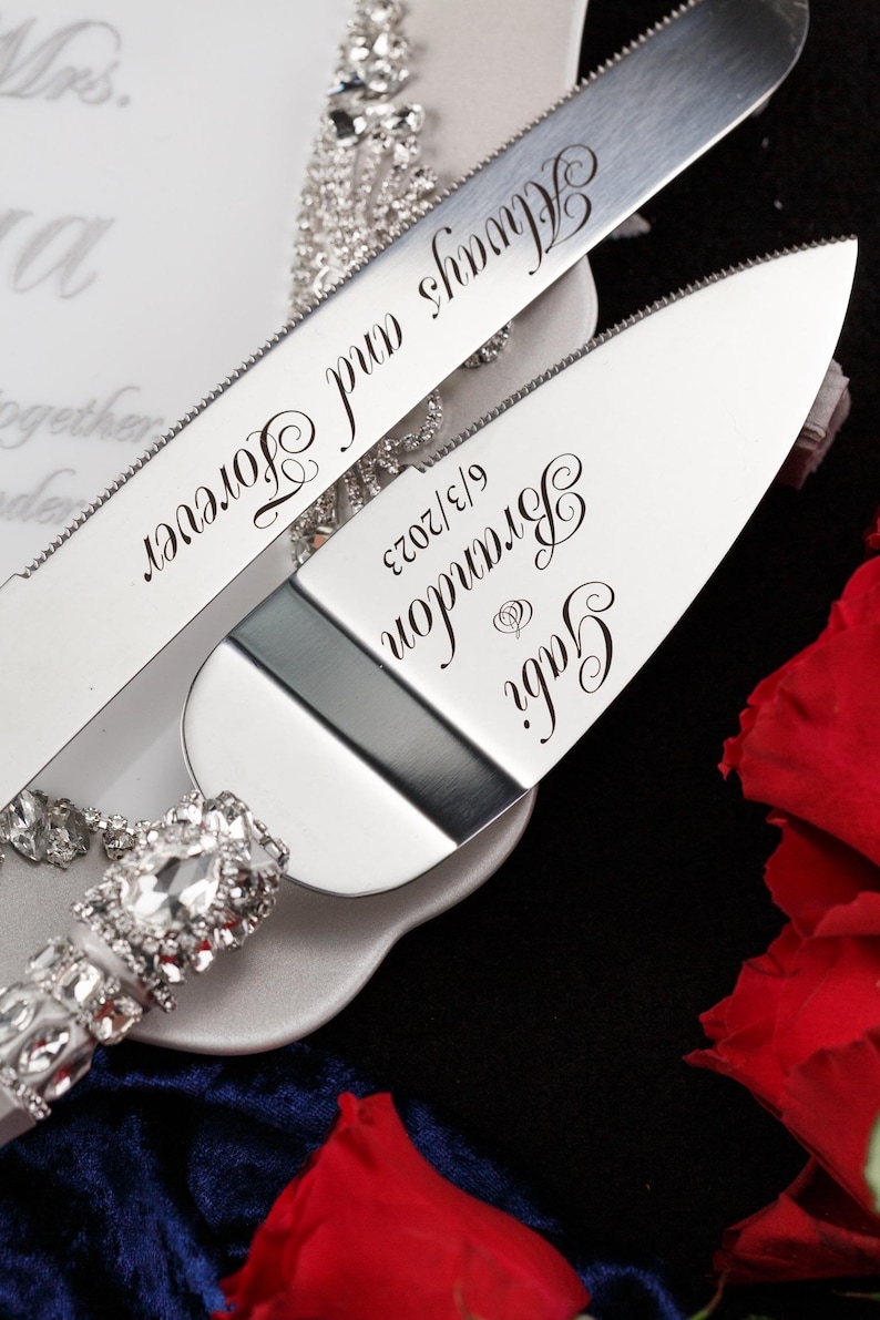 May include: A silver cake knife and server set with a rhinestone handle. The knife has the text "Always and Forever" engraved on it. The server has the text "Gary & Brianna 9/13/2023" engraved on it.