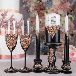 May include: Black wedding candle set with gold accents and rhinestones. The candle is decorated with the text "Mr. & Mrs. Holsinger 01.22.2023". Two black candle holders with rhinestones and two champagne flutes with gold and rhinestone accents.