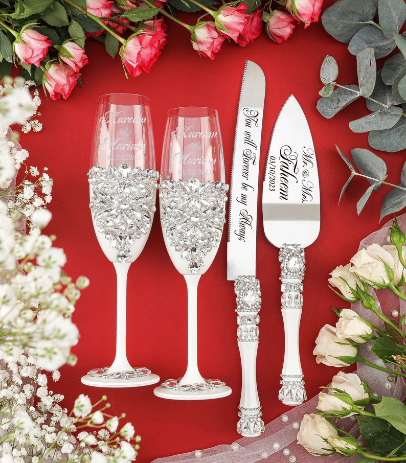 May include: Two champagne flutes and a cake knife with white handles and crystal embellishments. The flutes are engraved with the names "Karen & Marie" and the date "03/10/2023". The knife is engraved with "Mr. & Mrs. Faheem" and the date "03/10/2023". The knife also has the inscription "You will Forever be my Always".