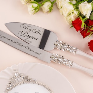 May include: A silver cake knife and server set with crystal-encrusted handles. The knife is engraved with the text All that you are is all that I'll ever need. The server is engraved with Mr. & Mrs. Bayomi and the date 26/10/26.