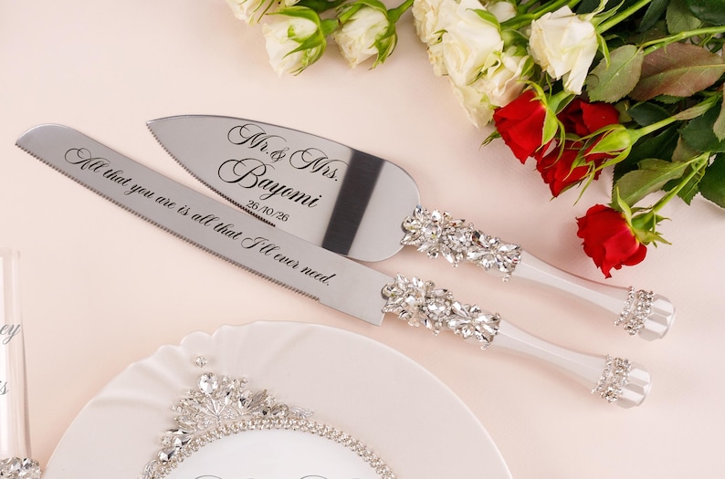 May include: A silver cake knife and server set with crystal-encrusted handles. The knife is engraved with the text All that you are is all that I'll ever need. The server is engraved with Mr. & Mrs. Bayomi and the date 26/10/26.