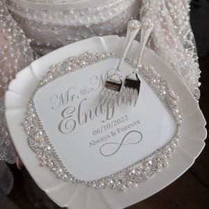 May include: White ceramic cake plate with a pearl and rhinestone border. The plate is engraved with the text "Mr. & Mrs.  Engaged 06/10/2022 Always & Forever" and features a silver infinity symbol. Two silver forks are placed on the plate.