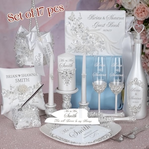 May include: A wedding ceremony set with 17 pieces, including a guest book, two champagne flutes, a champagne bottle, a cake knife and server, two candles, a pillow, a ring bearer pillow, and a decorative box. The set is decorated with rhinestones and the text "Brian & Shawna" and "Mr. & Mrs. Smith".
