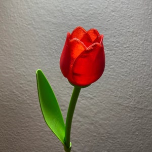 May include: A single red tulip with a green stem and leaf. The tulip is made of plastic and has a glossy finish.