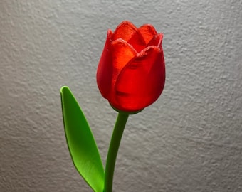 May include: A single red tulip with a green stem and leaf. The tulip is made of plastic and has a glossy finish.