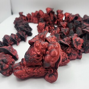 May include: A collection of 3D printed miniature figures in a red and black color scheme. The figures are arranged in a line and appear to be of a fantastical or sci-fi theme.