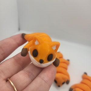 May include: A small orange fox figurine with a white face mask. The fox is curled up in a sleeping position.