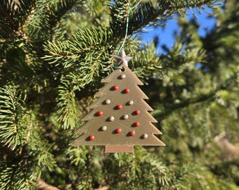May include: A Christmas tree ornament in the shape of a tree, decorated with red and white spherical ornaments. The ornament is suspended from a green string and hangs on a green pine tree branch. A star is at the top of the tree.