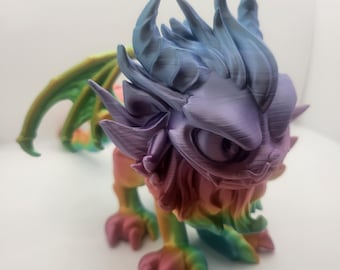 May include: A small, multi-colored, 3D printed dragon figurine with a spiky mane and wings. The dragon is standing on a white surface.