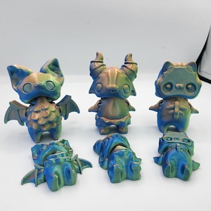 May include: Five small, iridescent, 3D printed figurines of fantastical creatures. The figures are a bat, a horned creature, a cat-like creature, and two smaller figures that appear to be parts of the larger figures.