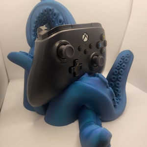 May include: A blue 3D printed octopus holding a black Xbox controller. The octopus has a textured surface and is holding the controller in its tentacles.