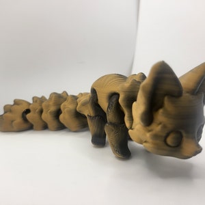 May include: A 3D printed figurine of a fox with a segmented tail. The figurine is brown and black and has a textured surface.