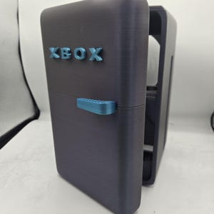 May include: A dark gray mini fridge with a blue handle and the word "XBOX" printed on the front.