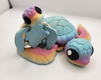 Puede incluir: Una colorida figura de tortuga impresa en 3D con una tortuga bebé en su espalda. La tortuga presenta un degradado arcoíris de colores, incluyendo azul, rosa, amarillo y morado. La figura tiene grandes ojos negros y un caparazón texturizado.