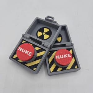May include: Two gray plastic boxes with a yellow and black striped design. Each box has a red button with the word "NUKE" printed in white. The top of one box is open, revealing a black and yellow radiation symbol.