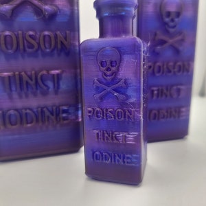 May include: Three purple glass bottles with a skull and crossbones design and the text "Poison Tinct Iodine" on each. The bottles are on a white surface.