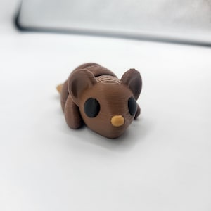 May include: A small brown 3D printed mouse figurine with black eyes and a yellow nose.