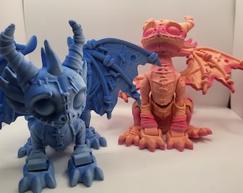 May include: Two small, 3D printed dragon figurines. One is blue and the other is pink. Both have stitched details and wings.