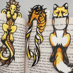 May include: Three colorful bookmarks featuring a yellow and orange seahorse, a yellow and orange dragon, and a yellow and orange fox. The bookmarks are made of paper and have a black outline.