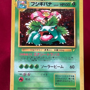 May include: A Pokémon trading card featuring the character Venusaur, a large, green, plant-like creature with a pink flower on its back. The card has Japanese text and a green and yellow border. The card's HP is 100.