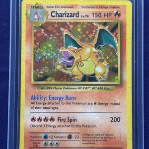 Puede incluir: Una carta Pokémon Charizard, etapa 2, con un fondo holográfico. La carta presenta una criatura naranja con forma de dragón y alas verdes. El texto de la carta incluye "Fire Spin" y "150 HP". La carta mide 170 cm de alto y pesa 90,5 kg.