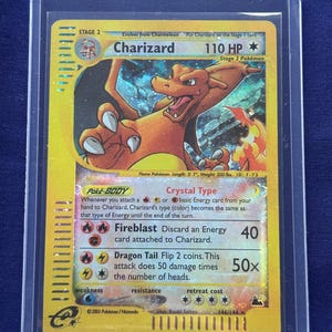 Może przedstawiać: Karta Pokémon Charizard, etap 2, w ochronnym etui. Karta przedstawia pomarańczową, smoczą istotę z płomieniami. Tekst zawiera "Charizard", "110 HP" i szczegóły ataku. Karta pochodzi z 2003 roku.