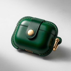 May include: A dark green protective case for wireless earbuds featuring a smooth finish, visible stitching along the edges, a central strap secured with a gold-toned metal snap button, and a matching gold-toned metal carabiner attached to the side.