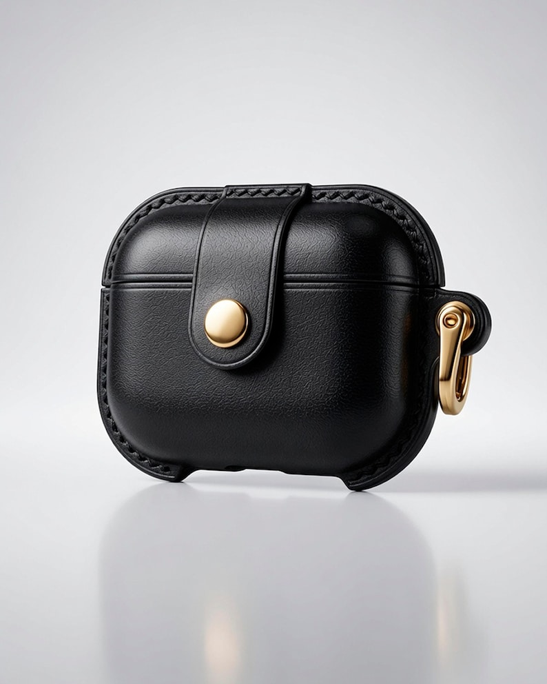 May include: A black protective case for wireless earbuds featuring a textured finish, a central vertical strap secured with a polished gold-tone snap button, and a matching gold-tone metal carabiner attached to the side for secure carrying.