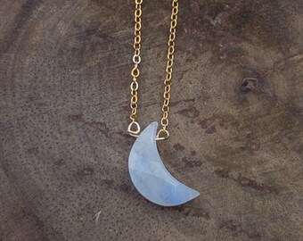 May include: A gold chain necklace with a crescent moon pendant made of white moonstone.