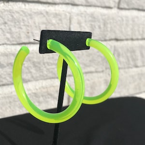 Puede incluir: Un par de pendientes grandes de aro de color verde neón. Los pendientes están hechos de plástico grueso y translúcido.