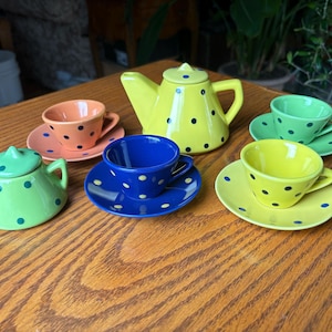 May include: A colorful ceramic tea set with a yellow teapot, two teacups, and two saucers. The set is decorated with black polka dots. The teacups and saucers are in shades of orange, green, yellow, and blue.