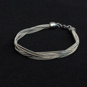 Könnte beinhalten: Silberarmband aus geflochtenen Gitarrensaiten.