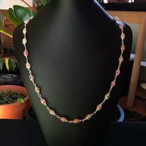 May include: A silver chain necklace with white oval beads with red and black speckles.