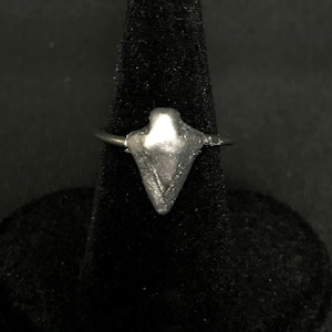 Op de afbeelding: Een zilveren ring met een puntig, driehoekig ontwerp. De ring ligt op een zwarte fluwelen standaard.