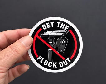 Può includere: Un adesivo circolare con sfondo nero e bordo bianco. Presenta la grafica di una telecamera di sicurezza solare su un palo, sbarrata da una linea diagonale rossa. Il testo GET THE FLOCK OUT è stampato in lettere maiuscole bianche.