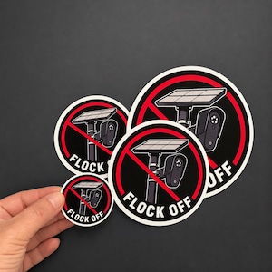 May include: Three circular stickers featuring a black and white illustration of a solar-powered security camera mounted on a pole. A red circle with a diagonal line overlays the camera. The text FLOCK OFF is printed in white at the bottom.