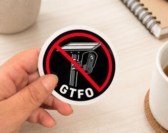 Può includere: Un adesivo circolare con sfondo nero e un simbolo di divieto rosso sopra la grafica di una telecamera di sicurezza montata su un palo con pannello solare. Il testo GTFO è stampato in lettere maiuscole bianche nella parte inferiore.