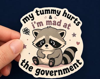 Può includere: Un adesivo fustellato raffigurante un procione dei cartoni animati con un'espressione triste, che si tiene la pancia. Il testo recita 'my tummy hurts & i'm mad at the government' in caratteri neri e viola, con piccole stelle e cuori.