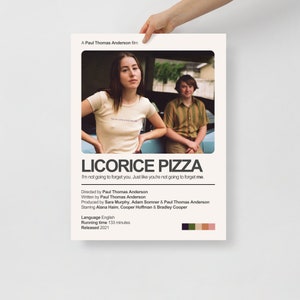 Può includere: Un poster del film "Licorice Pizza" tenuto da una persona. Il poster presenta una foto di due persone e il titolo del film. Il testo include il regista, lo sceneggiatore e il cast. La tavolozza dei colori del poster include beige, verde e marrone.