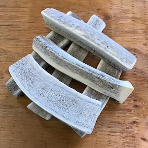 May include: Four natural white deer antlers, stacked on top of each other, with a light gray and white color. The antlers are smooth and have a natural texture.