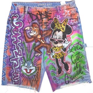 May include: Denim shorts with colorful graffiti art. The shorts feature cartoon characters, including a monkey, Bugs Bunny, and Minnie Mouse. The shorts have a distressed hem and the text "Let's Get it Crunk".
