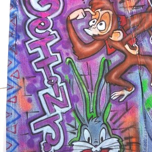May include: Denim shorts with a colorful graffiti design featuring cartoon characters and the text "Goth N' Love". The shorts have a distressed hem and the brand name "GEMMA RAE" is visible.