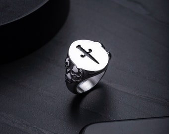 Peut inclure: Une bague en argent avec un motif de crâne et une découpe de poignard au centre de la bague.